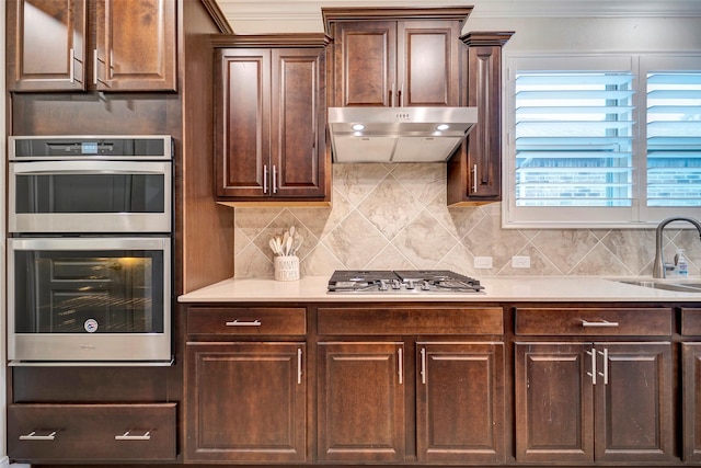 kitchen with backsplash, stainless steel appliances, dark brown cabinetry, and sink