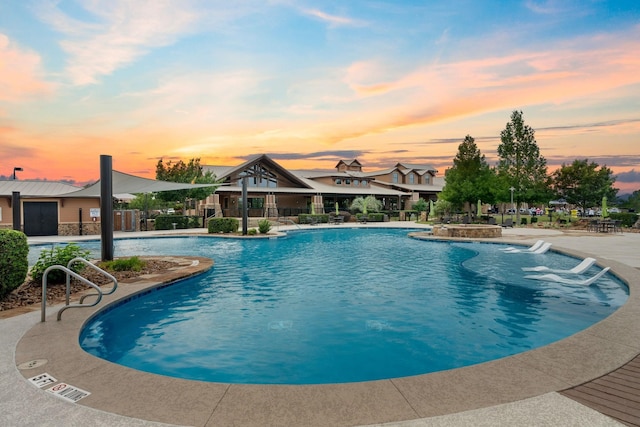 pool at dusk featuring pool water feature and a patio