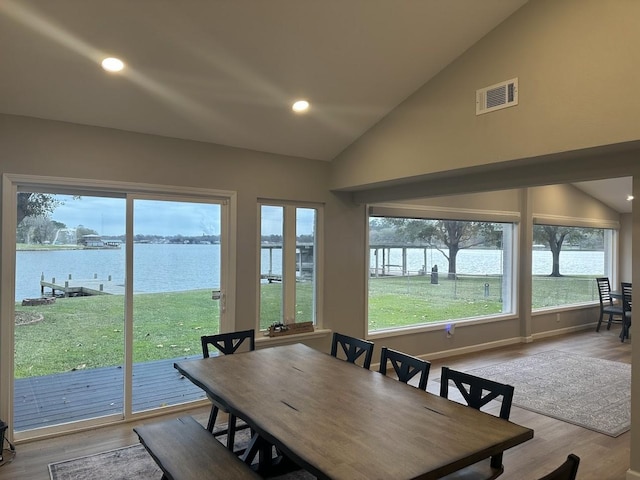 dining area with a water view, lofted ceiling, and light hardwood / wood-style flooring