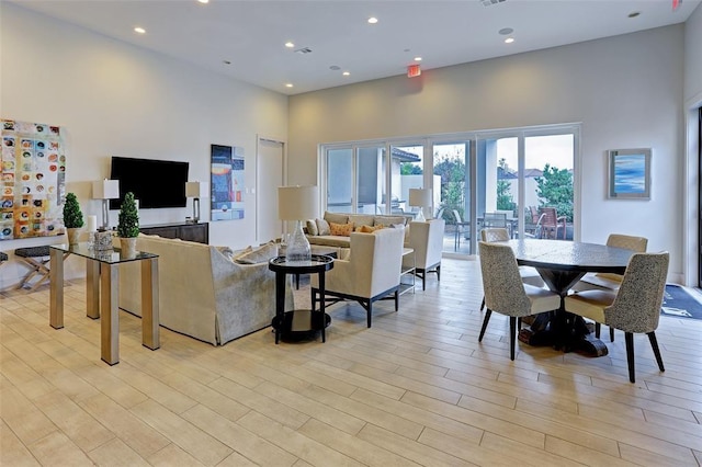 living area with light wood-style floors, recessed lighting, visible vents, and a towering ceiling