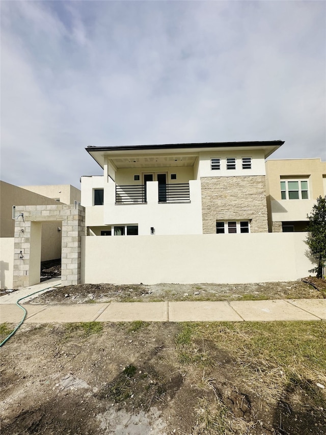 view of front of home with stone siding, fence, and stucco siding