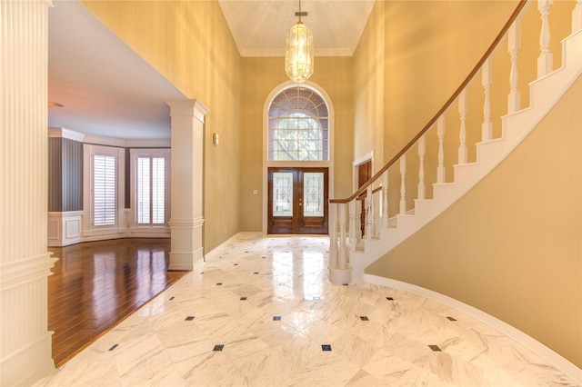 foyer entrance with french doors, decorative columns, crown molding, a chandelier, and wood-type flooring