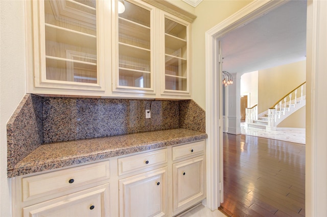 bar featuring light stone countertops, tasteful backsplash, light hardwood / wood-style flooring, a notable chandelier, and crown molding