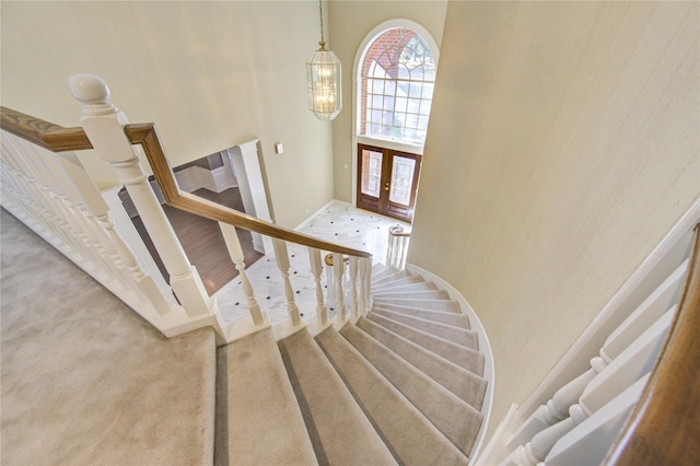 stairway with french doors, a towering ceiling, and a chandelier