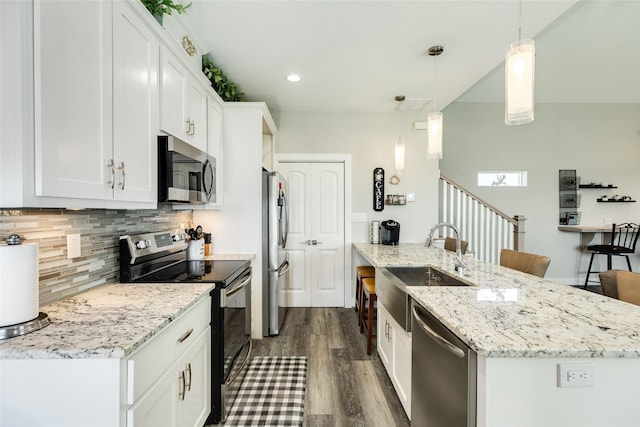 kitchen with light stone countertops, stainless steel appliances, a kitchen island with sink, decorative light fixtures, and white cabinets