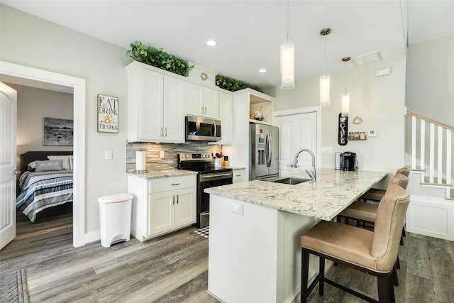 kitchen featuring kitchen peninsula, stainless steel appliances, sink, decorative light fixtures, and white cabinetry