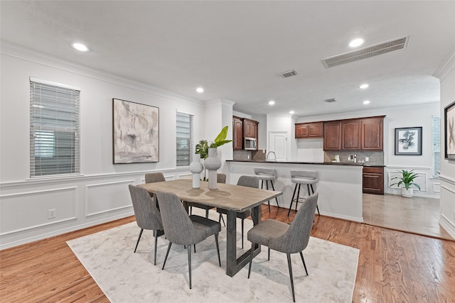 dining area with light hardwood / wood-style flooring, ornamental molding, and sink