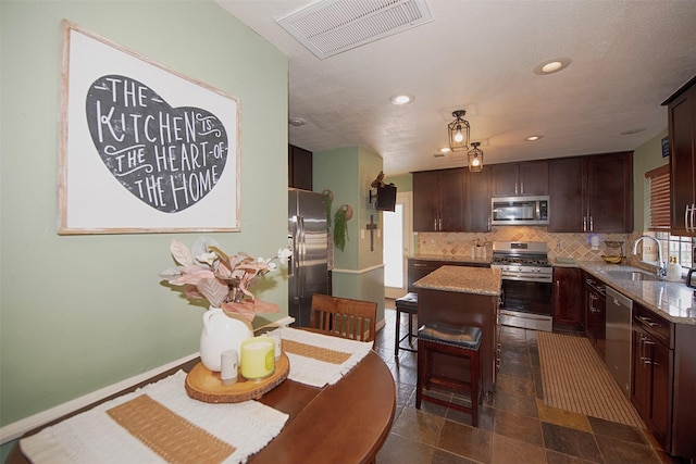 kitchen with sink, light stone counters, a center island, appliances with stainless steel finishes, and backsplash