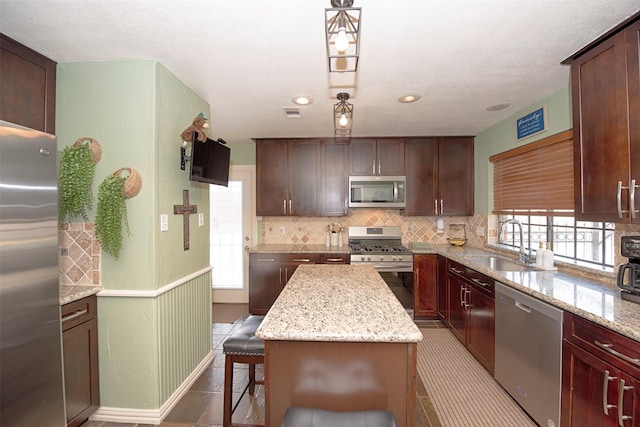 kitchen with sink, a kitchen island, stainless steel appliances, light stone countertops, and backsplash