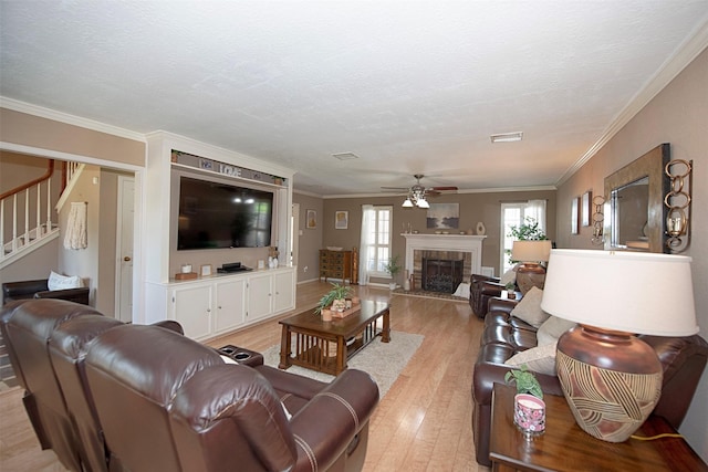 living room with a textured ceiling, light wood-type flooring, ornamental molding, ceiling fan, and a fireplace