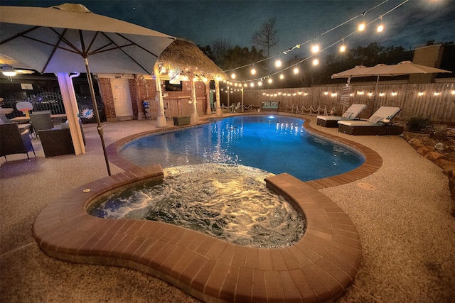 pool at twilight with an in ground hot tub and a patio