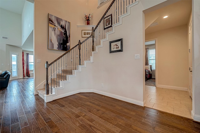 stairs featuring hardwood / wood-style floors, a healthy amount of sunlight, and a high ceiling