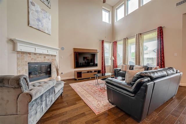 living room featuring a fireplace, plenty of natural light, dark wood-type flooring, and a high ceiling