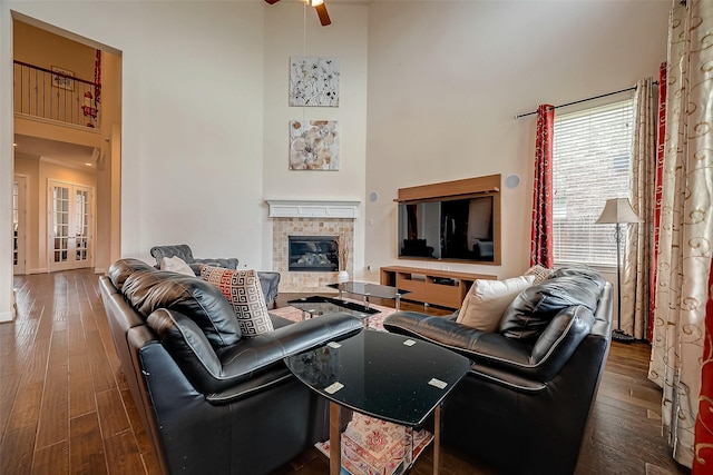 living room with a tile fireplace, ceiling fan, a high ceiling, and dark hardwood / wood-style floors