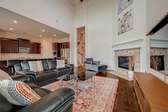 living room featuring a tile fireplace, a towering ceiling, and dark hardwood / wood-style flooring