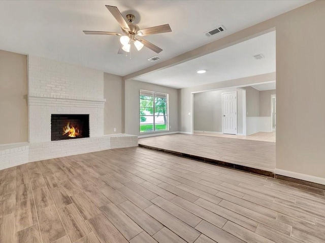 unfurnished living room with ceiling fan, light wood-type flooring, and a brick fireplace