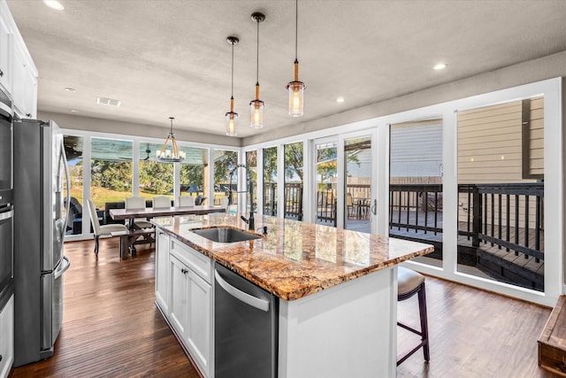 kitchen featuring a kitchen island with sink, white cabinets, stainless steel appliances, and light stone counters