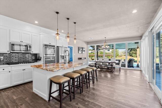 kitchen with white cabinets, a kitchen bar, stainless steel appliances, and an island with sink