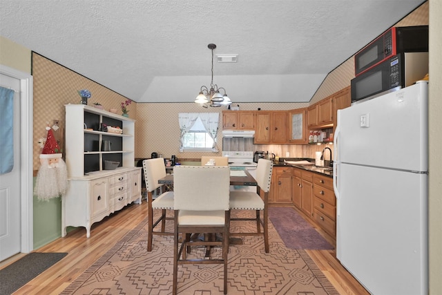 dining area featuring sink, a notable chandelier, a textured ceiling, vaulted ceiling, and light wood-type flooring