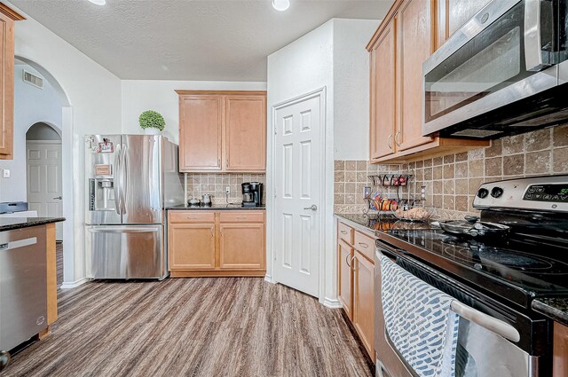 kitchen featuring light hardwood / wood-style floors, dark stone countertops, stainless steel appliances, and tasteful backsplash