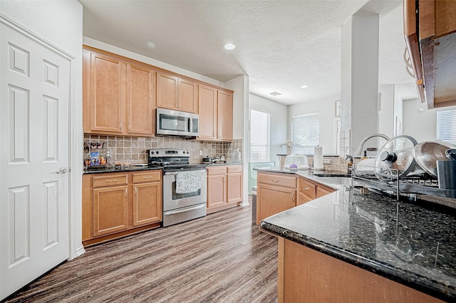 kitchen featuring decorative backsplash, appliances with stainless steel finishes, dark stone counters, sink, and hardwood / wood-style flooring