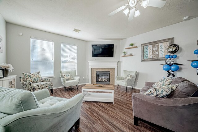 living room with a tile fireplace, wood-type flooring, and ceiling fan