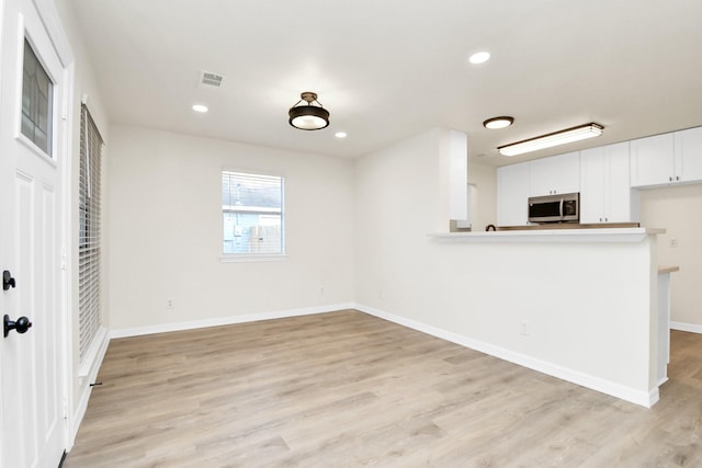 kitchen with kitchen peninsula, light wood-type flooring, and white cabinetry