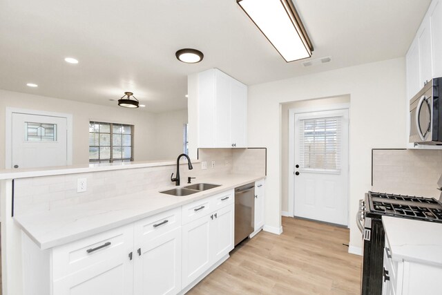 kitchen featuring sink, decorative backsplash, light stone counters, white cabinetry, and stainless steel appliances