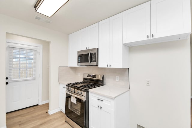 kitchen with backsplash, light stone countertops, appliances with stainless steel finishes, light hardwood / wood-style floors, and white cabinetry