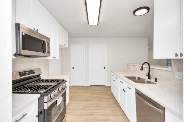 kitchen with white cabinets, sink, appliances with stainless steel finishes, light hardwood / wood-style floors, and light stone counters