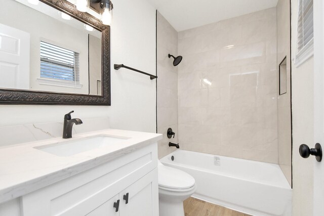 full bathroom featuring hardwood / wood-style floors, tiled shower / bath combo, toilet, and vanity