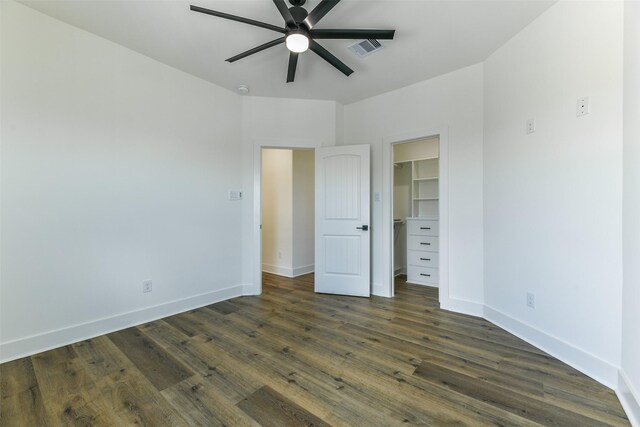 unfurnished bedroom with ceiling fan, a spacious closet, dark wood-type flooring, and a closet