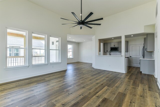 unfurnished living room with ceiling fan, dark hardwood / wood-style flooring, and high vaulted ceiling