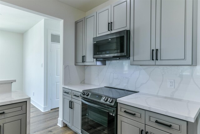 kitchen featuring light stone countertops, black range with electric cooktop, light hardwood / wood-style flooring, and backsplash