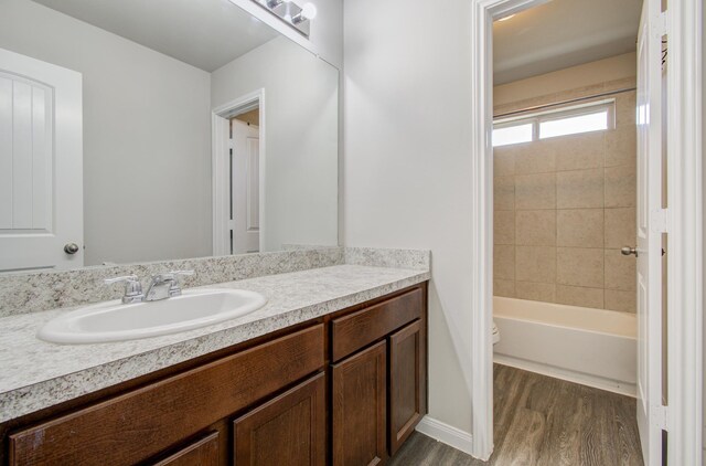 full bathroom with hardwood / wood-style floors, vanity, tiled shower / bath combo, and toilet