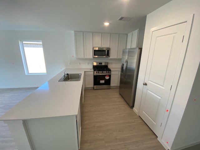 kitchen with kitchen peninsula, appliances with stainless steel finishes, sink, white cabinets, and light hardwood / wood-style floors