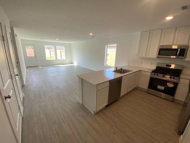 kitchen featuring light countertops, appliances with stainless steel finishes, a peninsula, light wood-style floors, and a sink