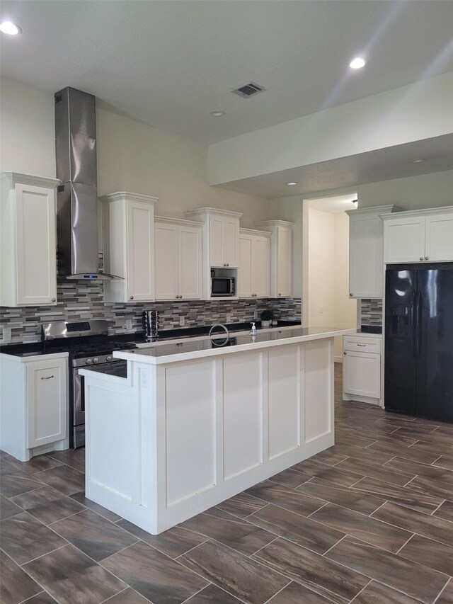 kitchen featuring a center island with sink, black fridge, wall chimney exhaust hood, built in microwave, and stainless steel range oven