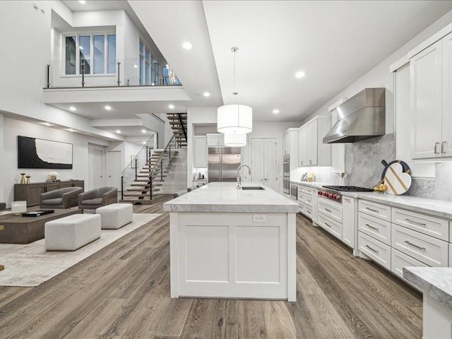 kitchen featuring white cabinets, stainless steel appliances, hanging light fixtures, and wall chimney exhaust hood