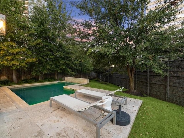 pool at dusk featuring a patio and a lawn