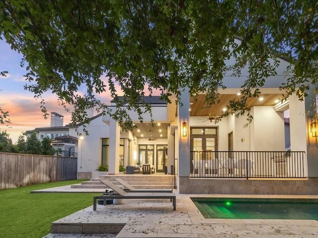 back house at dusk featuring ceiling fan, a patio area, a fenced in pool, and a yard