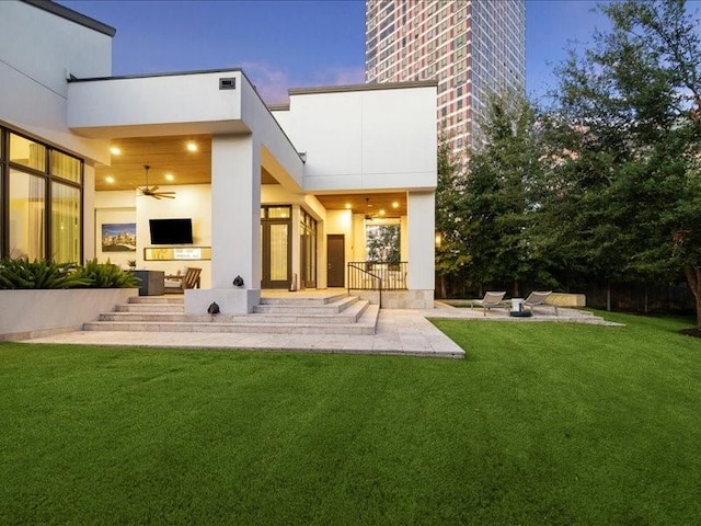 back house at dusk with a lawn, a patio area, and ceiling fan