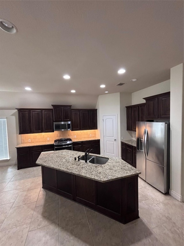 kitchen featuring dark brown cabinetry, sink, stainless steel appliances, tasteful backsplash, and a kitchen island with sink