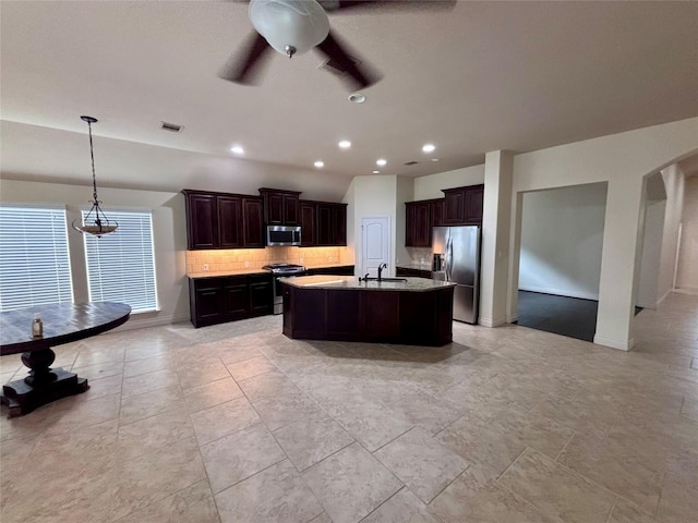 kitchen with sink, stainless steel appliances, tasteful backsplash, an island with sink, and pendant lighting