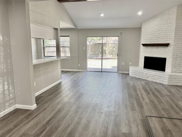 unfurnished living room featuring dark hardwood / wood-style flooring, vaulted ceiling, and a brick fireplace