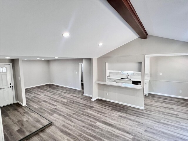 unfurnished living room featuring hardwood / wood-style floors, vaulted ceiling with beams, and sink