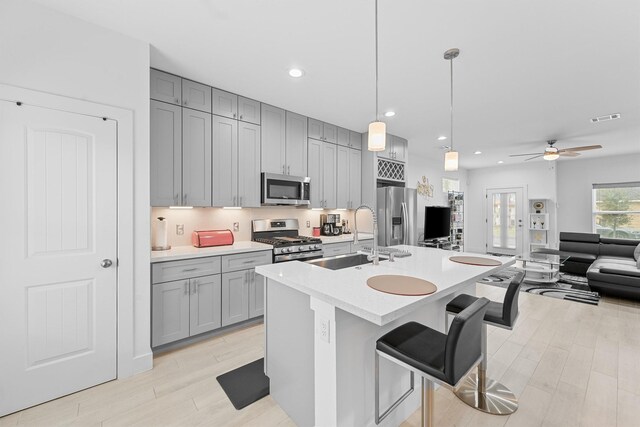 kitchen with a breakfast bar, stainless steel appliances, ceiling fan, sink, and decorative light fixtures