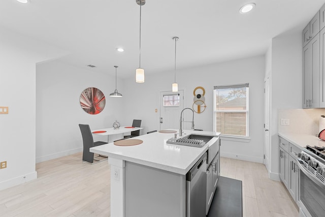 kitchen featuring pendant lighting, a kitchen island with sink, sink, gray cabinets, and appliances with stainless steel finishes