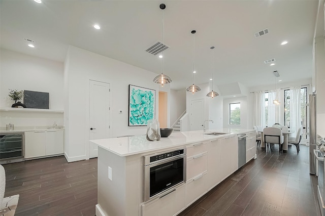 kitchen with decorative light fixtures, a center island with sink, sink, white cabinetry, and appliances with stainless steel finishes