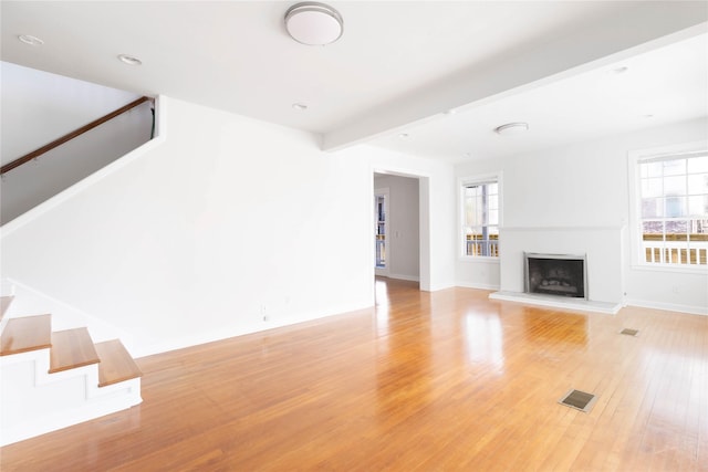 unfurnished living room featuring beam ceiling, plenty of natural light, and light hardwood / wood-style floors